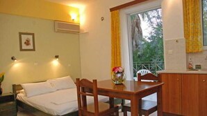 A room with a bed, wooden table, chairs, a window with curtains, a small kitchen area, and a picture on the wall.
