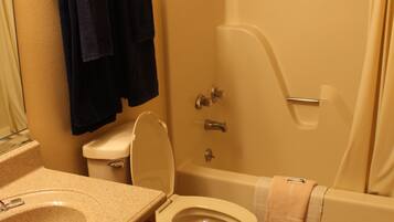 Une salle de bain avec des toilettes, un lavabo et une baignoire. Des serviettes sont accrochées au mur et il y a un rideau de douche.