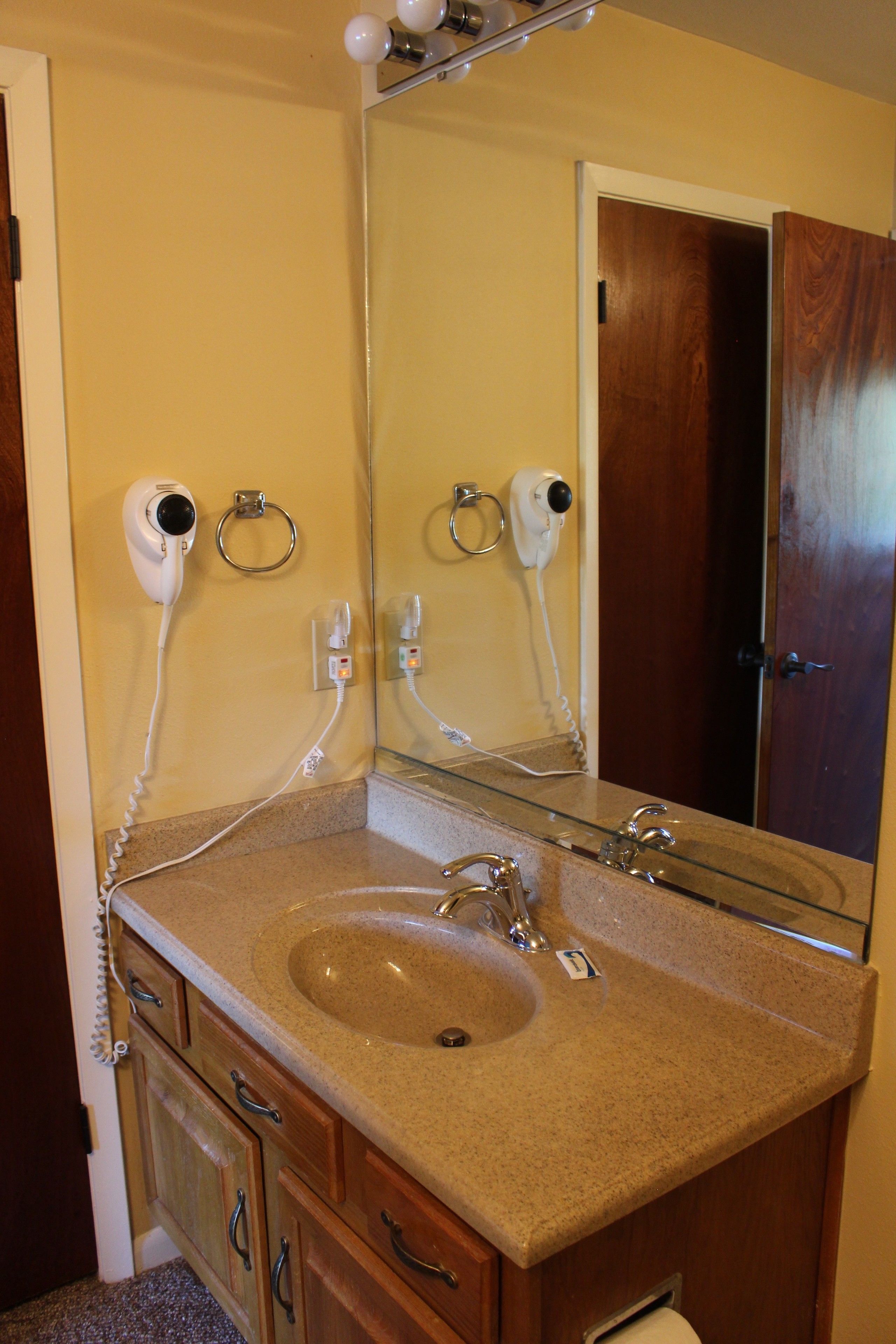 Une salle de bain équipée d’un lavabo, d’un miroir et de sèche-cheveux fixés au mur.