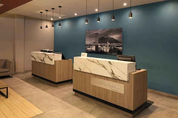 A hotel reception area with marble countertops, wooden reception desks, and a cityscape painting on the wall. - City Express Plus by Marriott Monterrey Galerias (Monterrey)