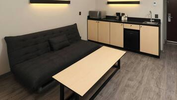 Un espacio habitable pequeño con sofá, una mesita, kitchenette y una puerta.
