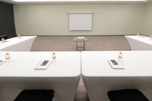 A conference room with four tables, each with a water bottle and a notebook. A projector is on a table in the center.