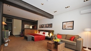 A modern hotel room with a large bed, a sofa, a coffee table, and a dining table. There is a large window, a mirror, and a picture on the wall. - Belgrade Boutique House (Belgrade)