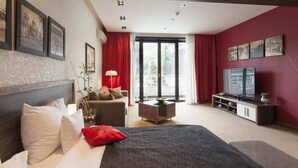 A modern hotel room with a large bed, a sofa, a TV, and a balcony with red curtains. - Belgrade Boutique House (Belgrade)