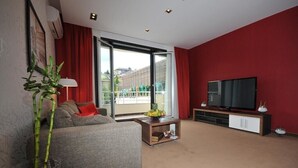 A living room with a sofa, a television, a sliding glass door, and a red wall. - Belgrade Boutique House (Belgrade)