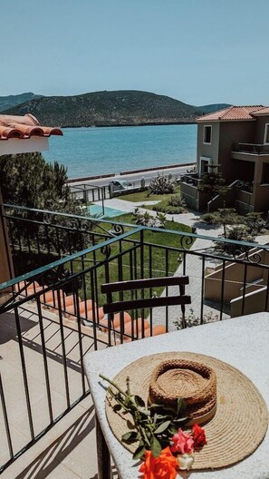 Un balcone con vista sull'acqua e sulle colline, un cappello di vimini e fiori su un tavolo.