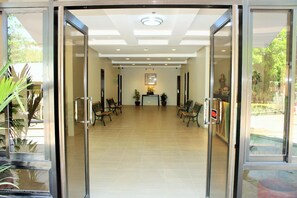 A reception area with a glass door, a reception desk, several chairs, and potted plants. - Coron Visitors Hotel (Coron)