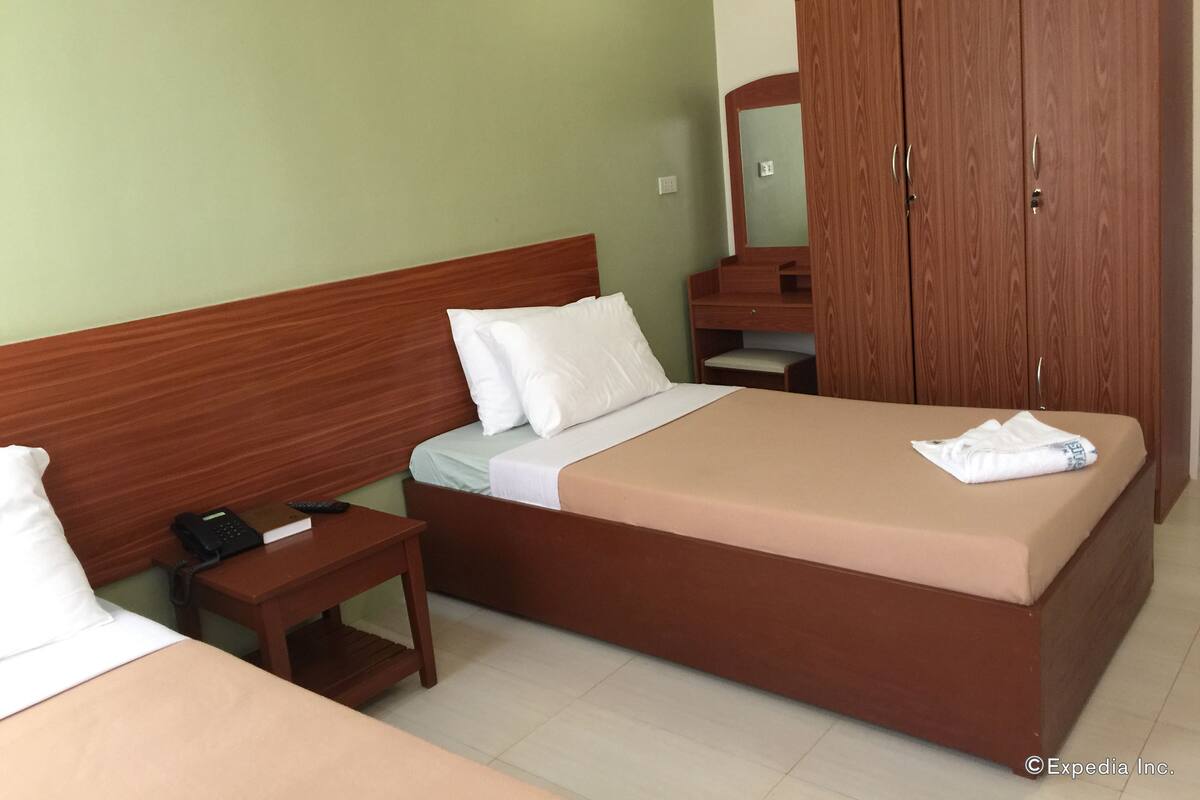 A hotel room with a wooden bed, a bedside table with a phone, a mirror, and a wardrobe.