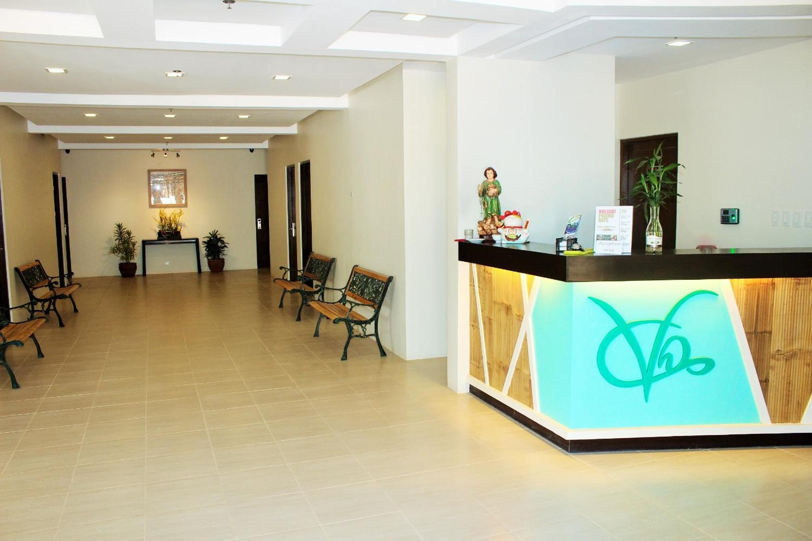 A hotel reception area with a reception desk, several wooden benches, and potted plants.