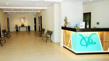 A hotel reception area with a reception desk, several wooden benches, and potted plants.