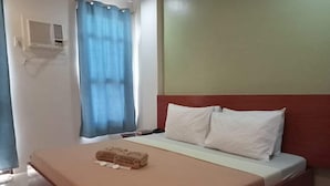 A neatly made bed with a brown bedspread and two white pillows, a blue curtain, and a wall-mounted air conditioning unit. - Coron Visitors Hotel (Coron)