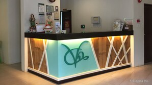A reception desk with a wooden finish and a teal logo, surrounded by various informational posters and a clock on the wall. - Coron Visitors Hotel (Coron)