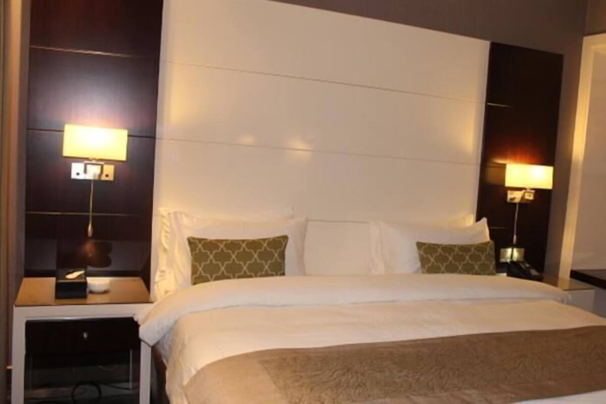 Une chambre d’hôtel avec un grand lit, deux tables de chevet et deux lampes fixées au mur.