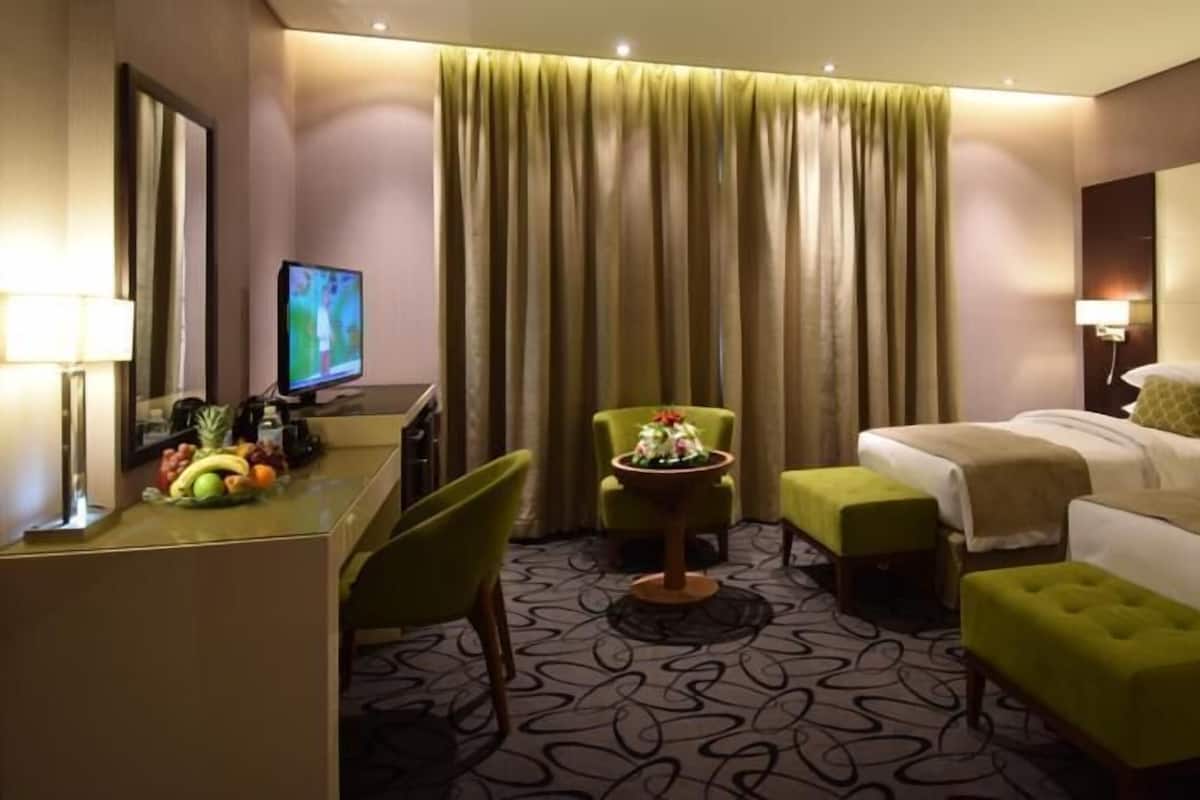 Une chambre d’hôtel avec un lit, un bureau avec un ordinateur, une chaise, une petite table avec des fleurs et un téléviseur.