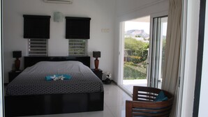 A bedroom with a bed, two bedside lamps, a nightstand, a window with curtains, and a view of greenery and mountains. - Sun Sea Sleep B&B (Willemstad)