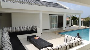 A modern outdoor living area with a pool, white furniture, and a covered patio. - Sun Sea Sleep B&B (Willemstad)