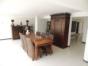 A dining area with a wooden table and wicker chairs, a dark wooden cabinet, and a tiled floor. - Sun Sea Sleep Apartments (Willemstad)