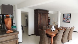 A dining area with a wooden table and wicker chairs, a large cabinet, and a painting on the wall. - Sun Sea Sleep Apartments (Willemstad)