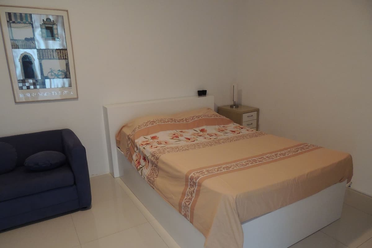 A bedroom with a bed, a nightstand, a lamp, and a framed picture on the wall.
