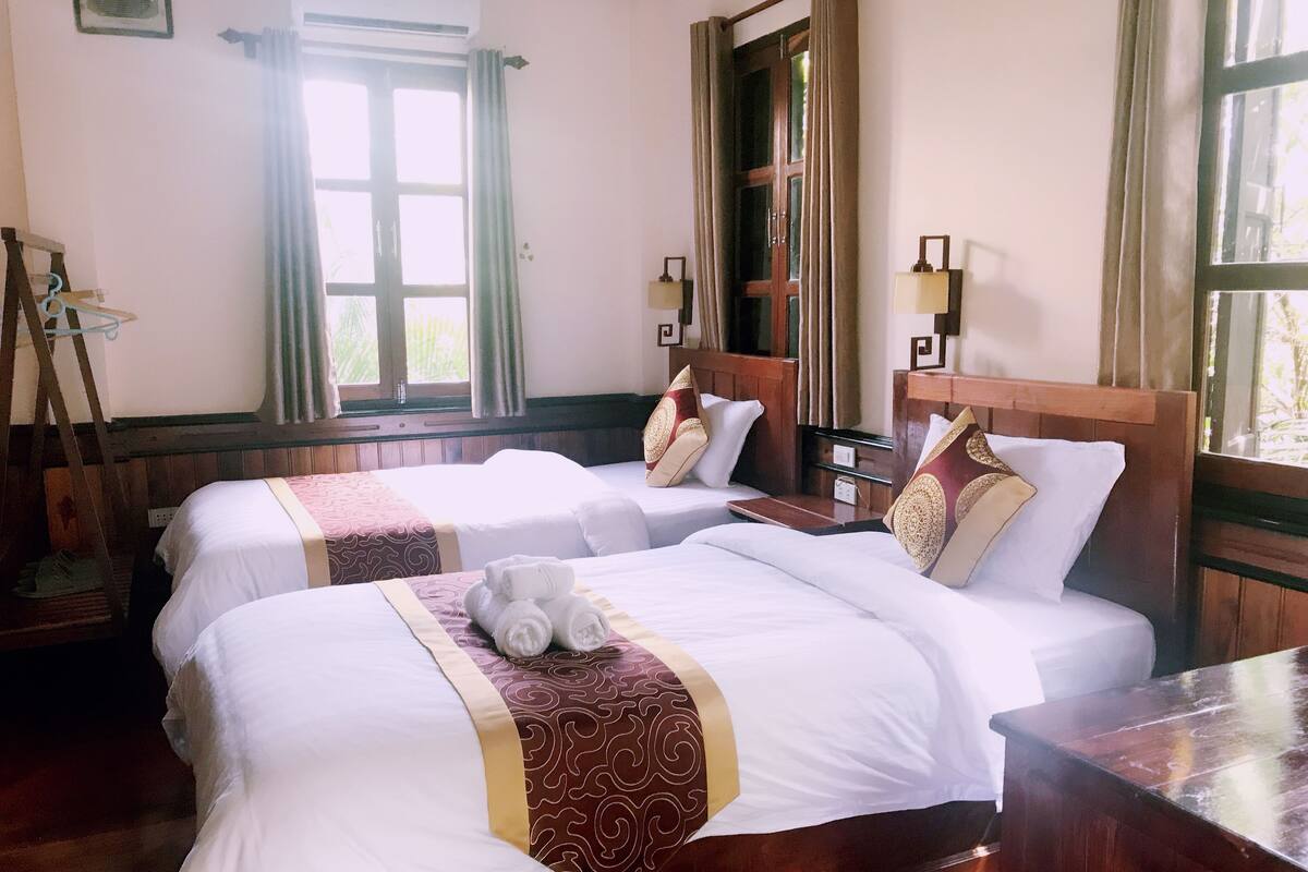 A hotel room with two beds, a wooden headboard, a wooden desk, and a window with curtains.