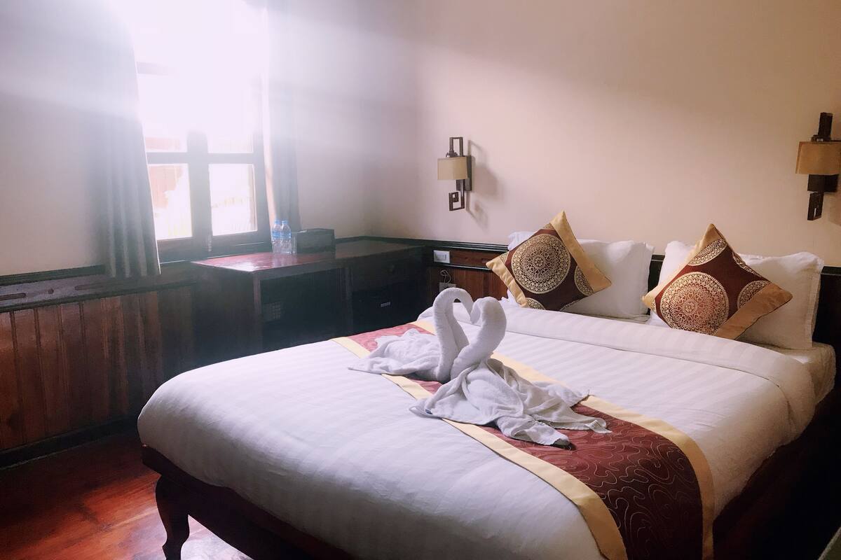 A hotel room with a large bed, two wall-mounted lamps, a wooden desk, and a window with curtains.