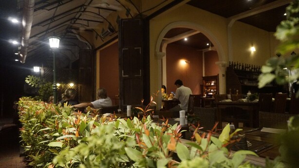 Un comedor interior con mesas y sillas, una zona de bar con botellas, y una persona trabajando detrás de la barra.