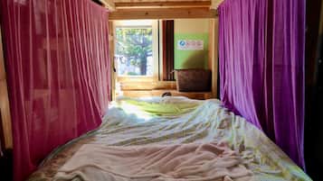 A narrow room with a bed, purple curtains, a window, and a green wall with a sign.
