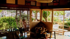 Una habitación japonesa tradicional con suelo de tatami, una mesa de madera baja, una silla y un ventanal con vistas a la vegetación.