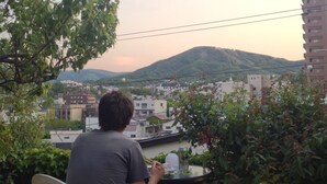 Una persona sentada a una mesa con vista a un paisaje urbano y colinas al fondo.