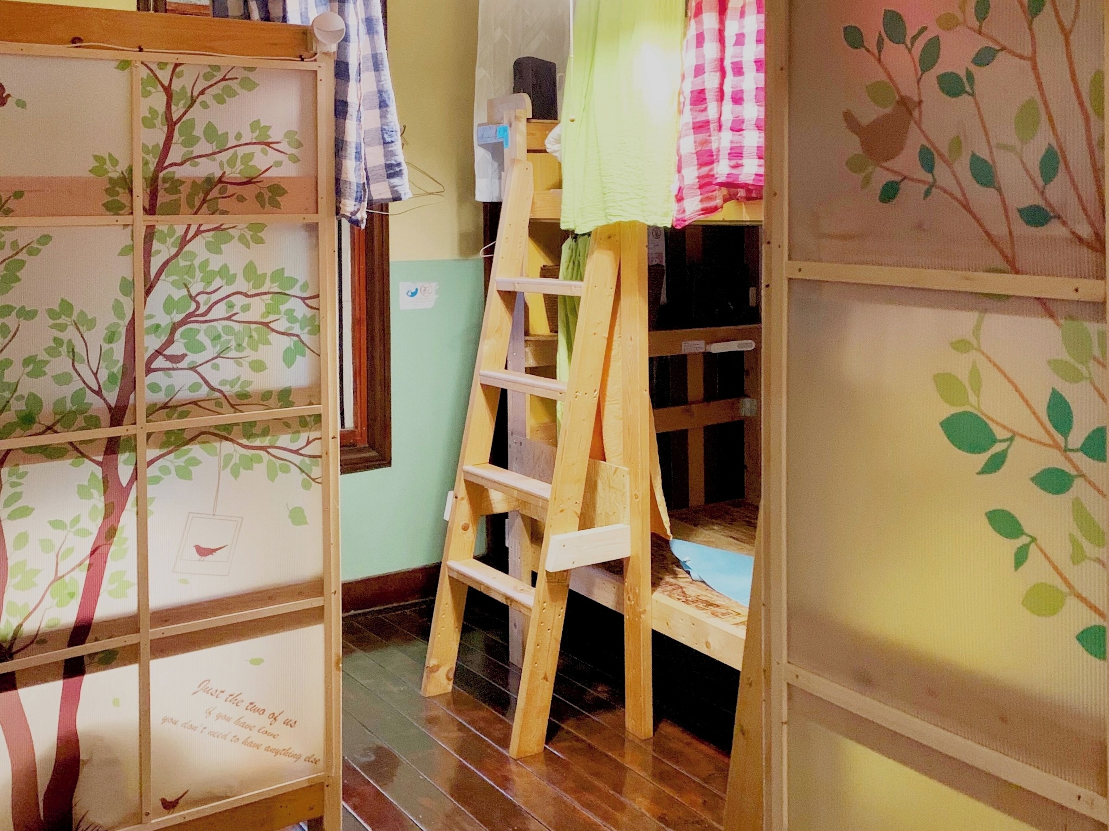 Een kamer met een houten ladder, een raam met uitzicht en een muur met een boommotief.