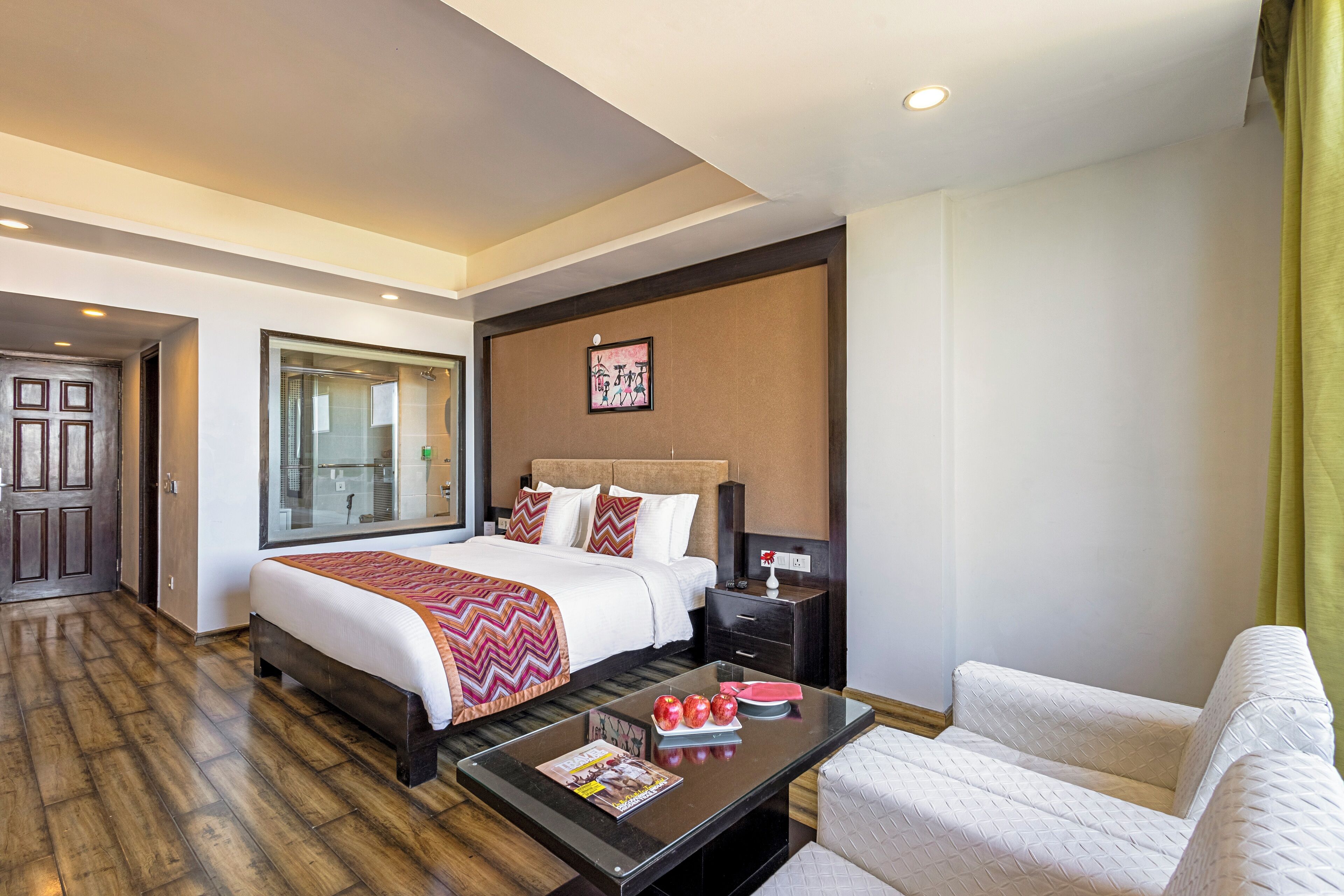 A hotel room with a large bed, a bedside table with a lamp, a sofa, and a large window.