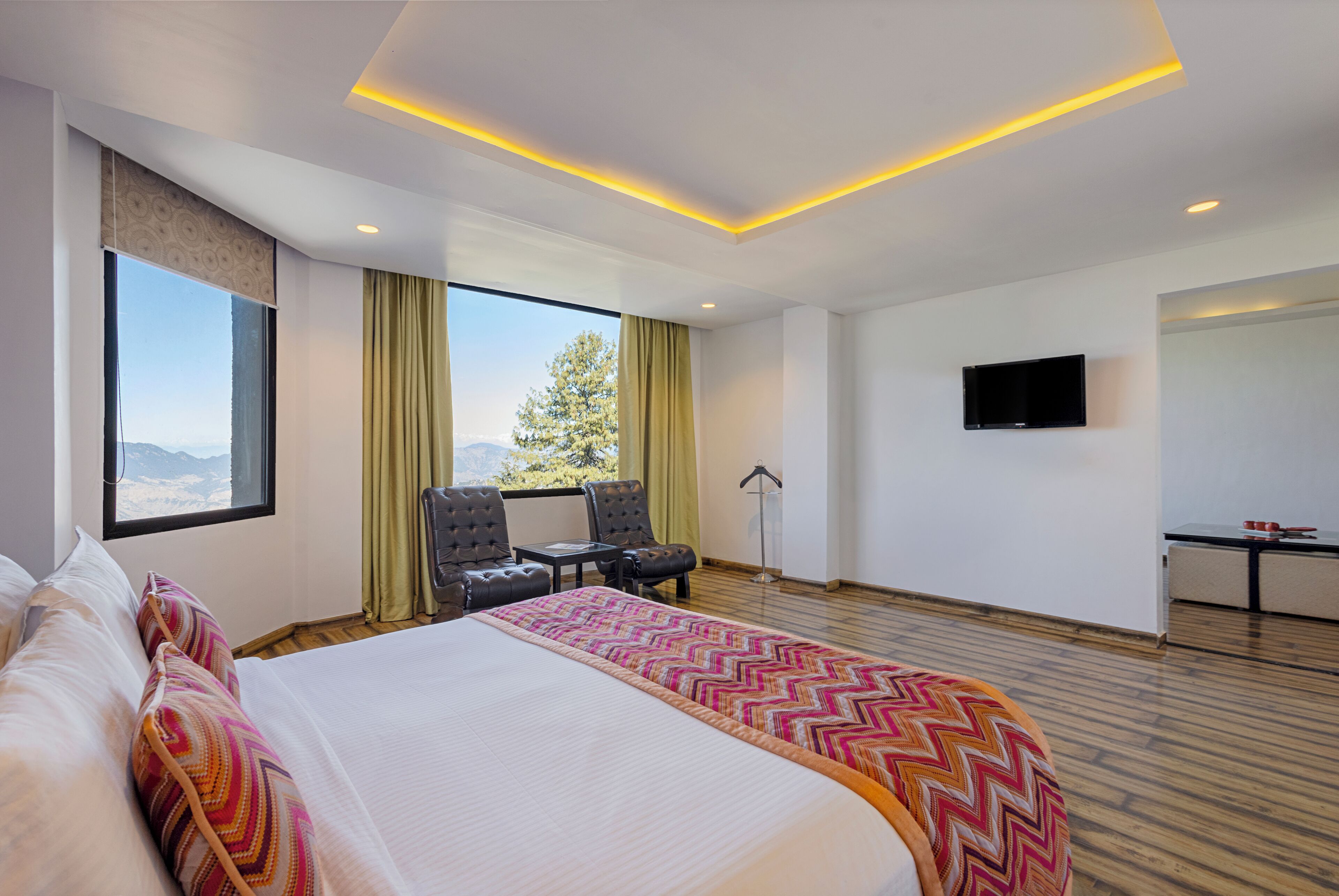 A modern hotel room with a large bed, a desk, a chair, a television, and a view of the outdoors.