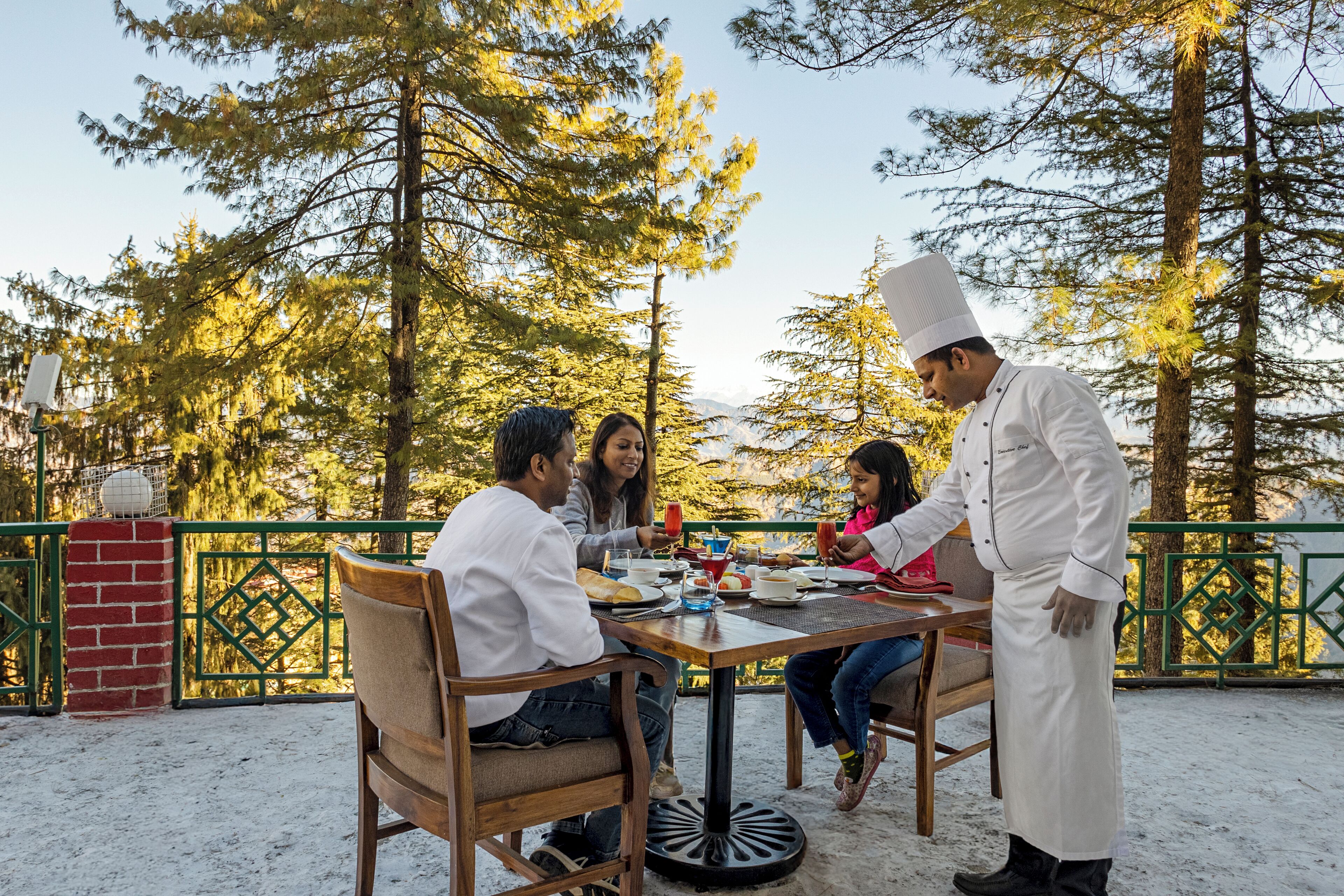 A group of people dining outdoors at a table with a chef serving food.