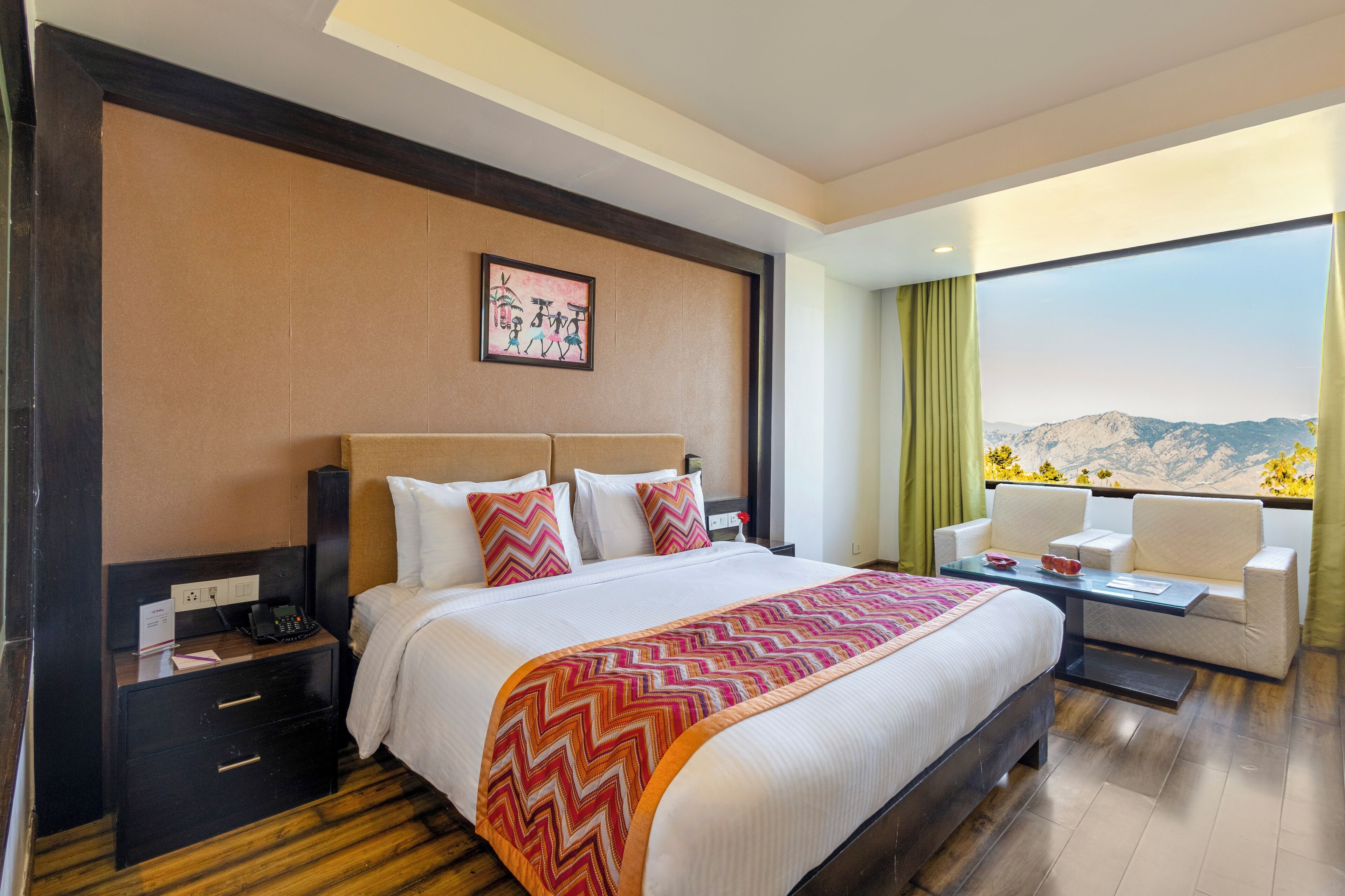 Une chambre d’hôtel avec un grand lit, un bureau avec une chaise, une table de chevet et une vue sur les montagnes par la fenêtre.