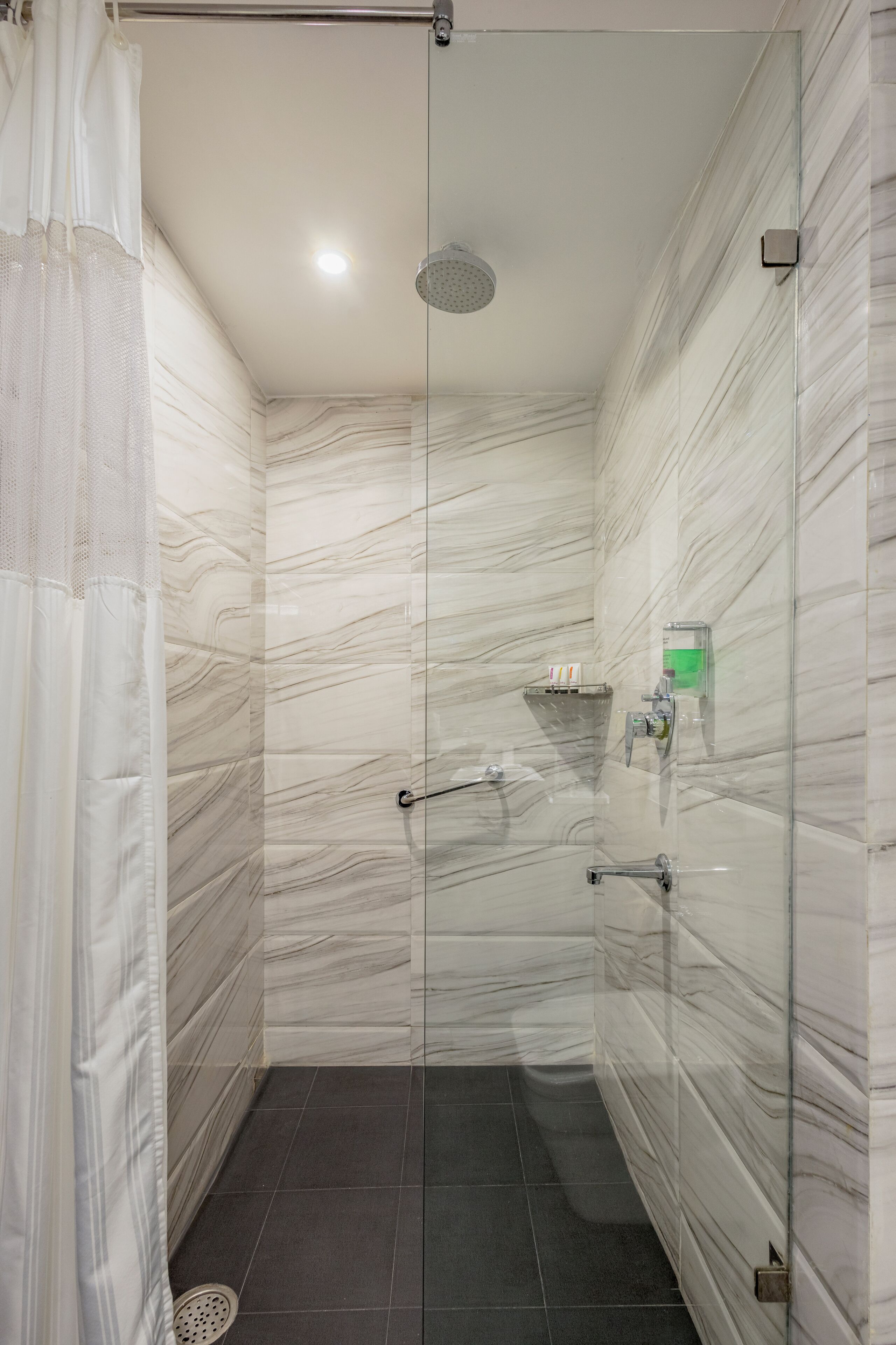 Une douche moderne dotée d’une porte en verre, de murs en marbre et d’une petite étagère pour les articles de toilette.