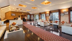 A spacious lobby with modern furniture, a red patterned rug, and wooden ceiling panels. - Sterling Kufri (Theog)