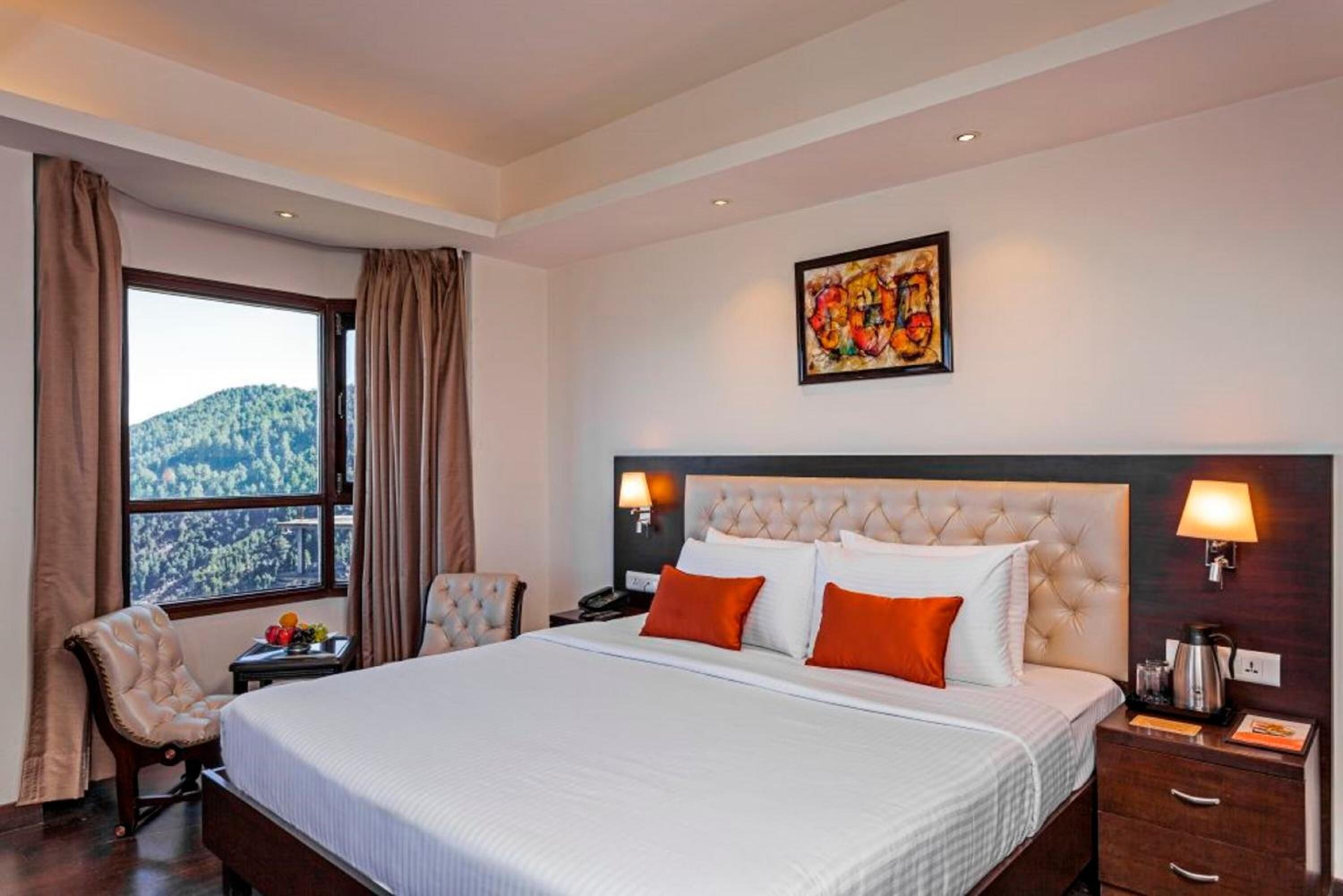 A hotel room with a large bed, two bedside tables, a chair, a window with curtains, and a painting on the wall.