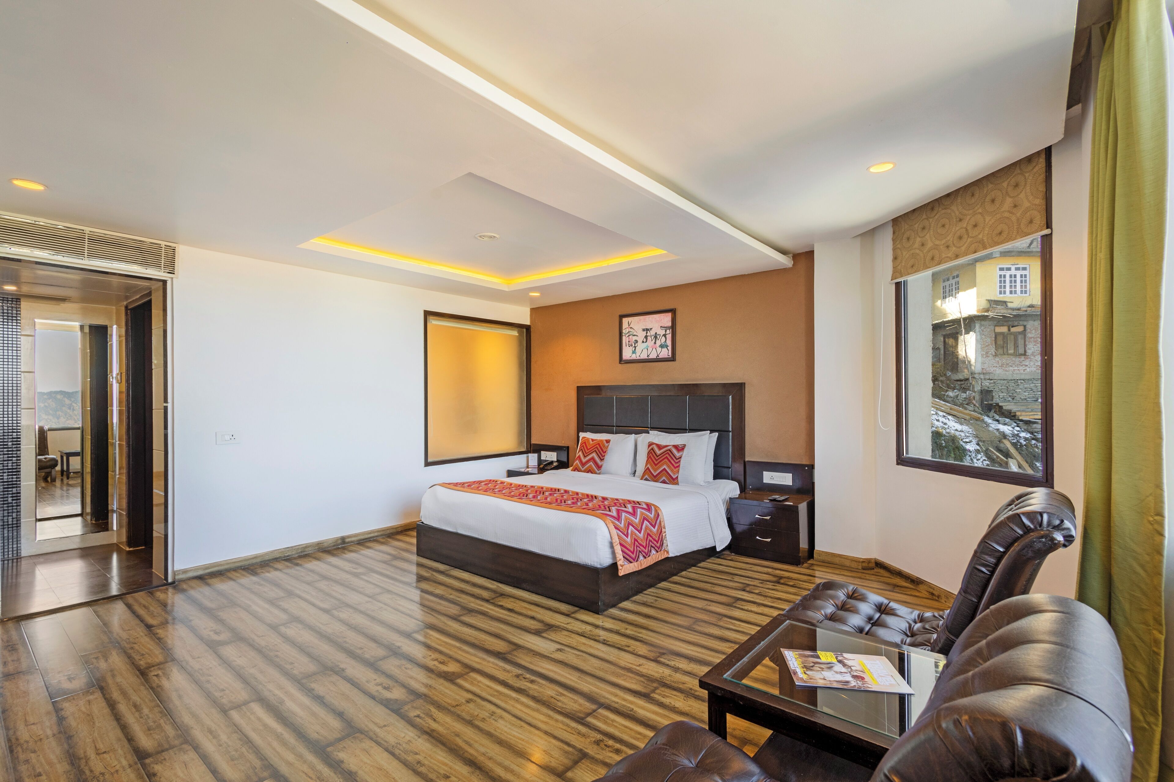 Une chambre d’hôtel moderne avec un grand lit, un canapé en cuir et une vue sur un paysage enneigé par la fenêtre.