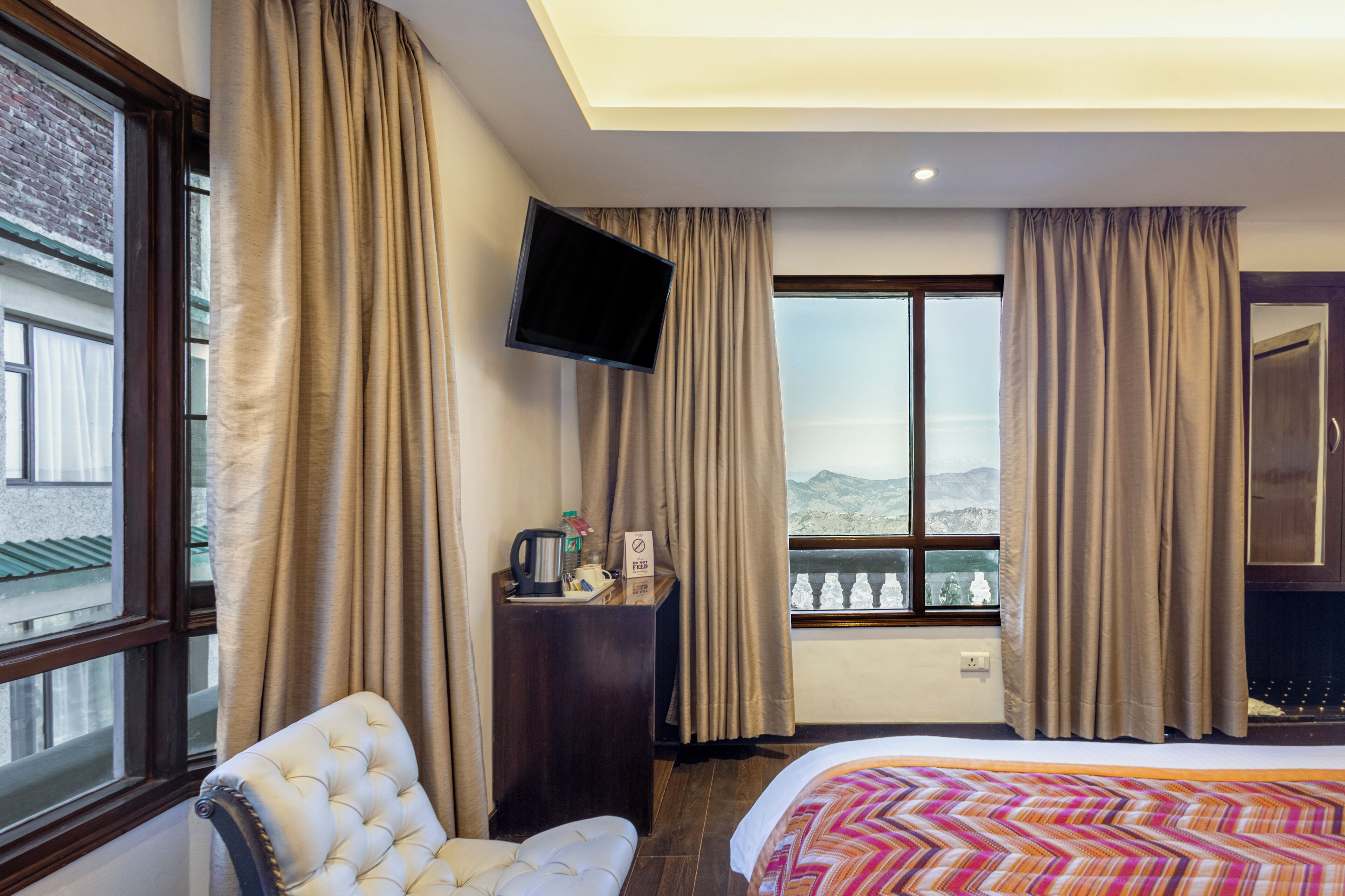 A hotel room with a bed, a chair, a desk with a flat-screen TV, and a window with curtains.