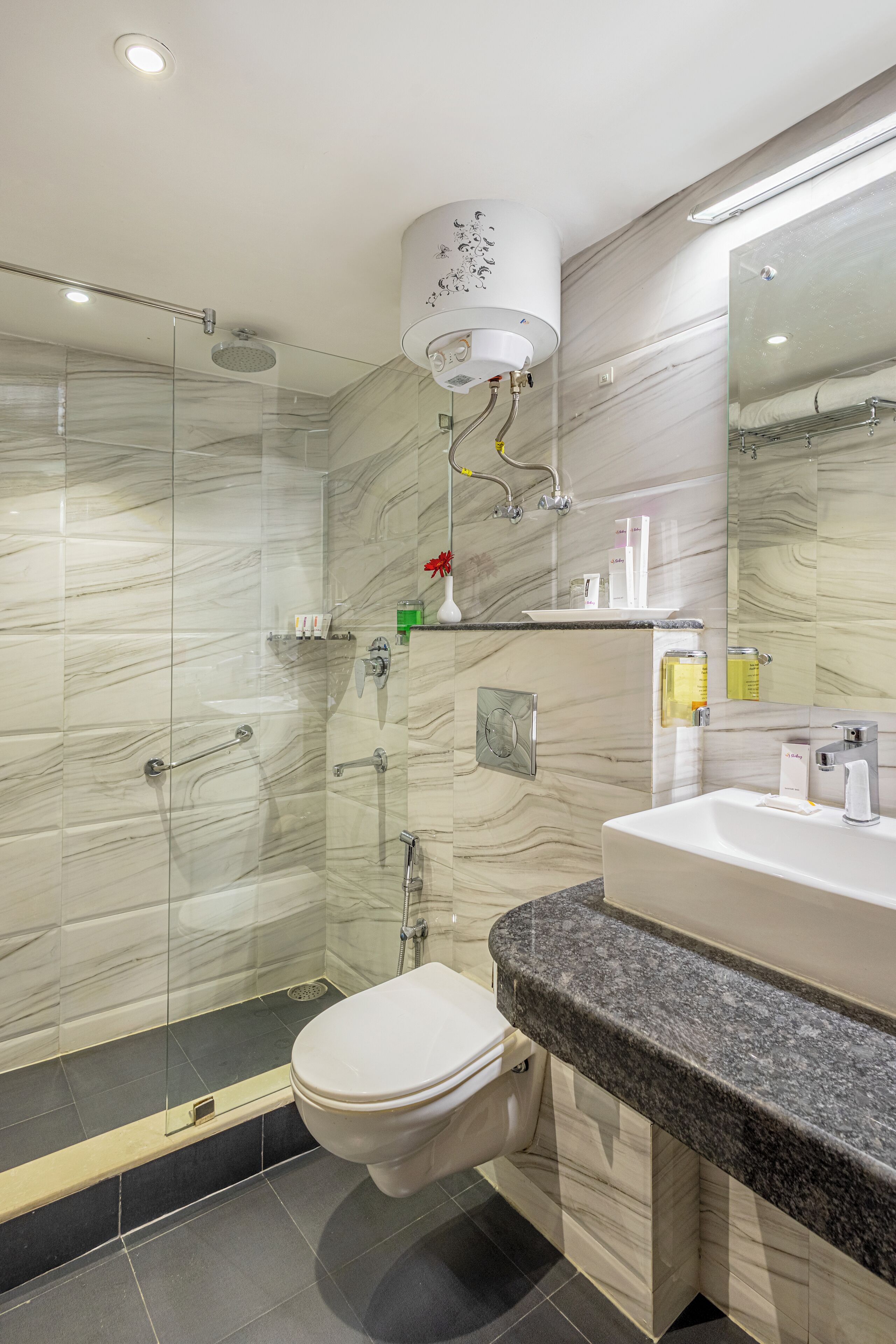 Un bagno moderno con doccia vetrata, un water bianco, un piano di lavoro in granito e una parete di fondo in marmo.