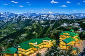 A hotel with multiple buildings, green roofs, and a mountainous backdrop. - Sterling Kufri (Theog)
