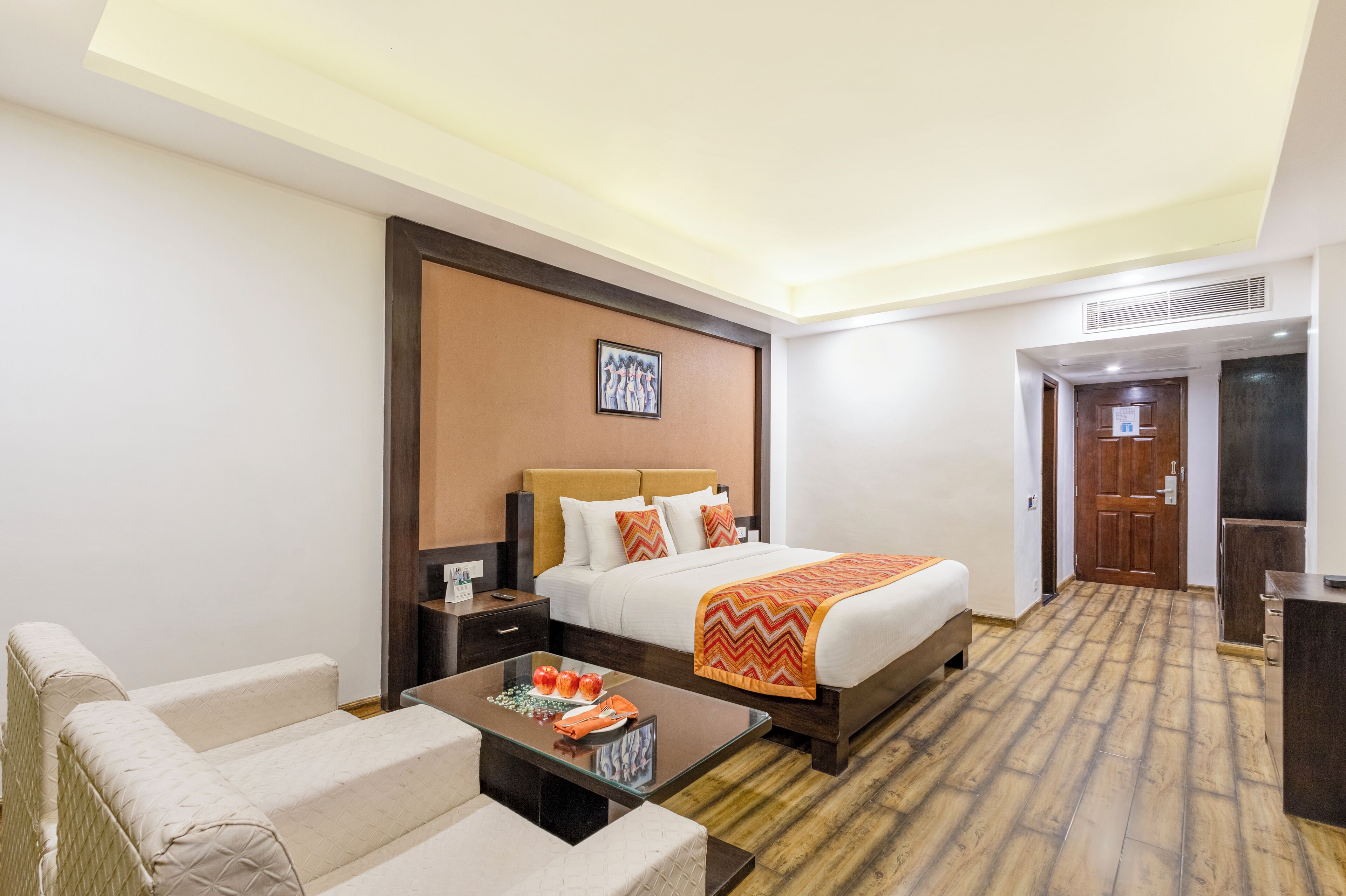 A hotel room with a bed, a sofa, a coffee table, a nightstand, and a wooden floor.