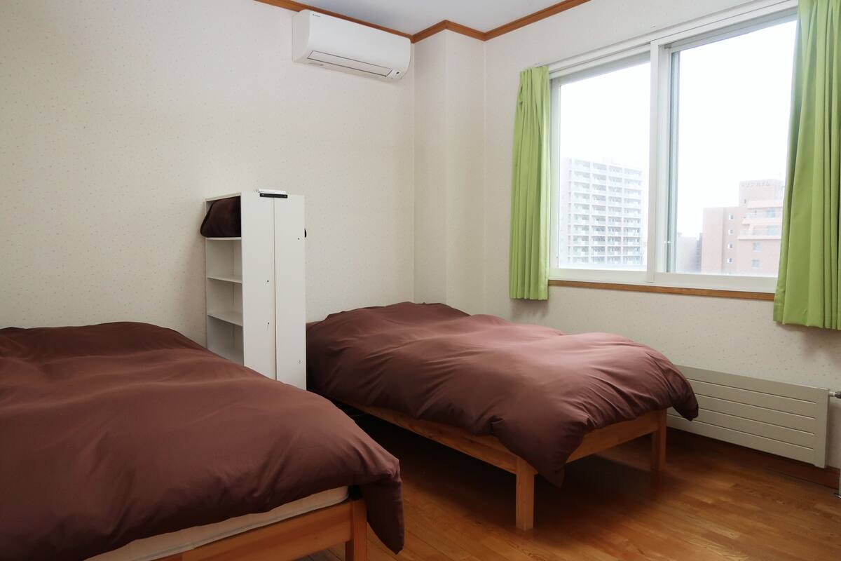 A room with two single beds, a wardrobe, a radiator, and a window with curtains.