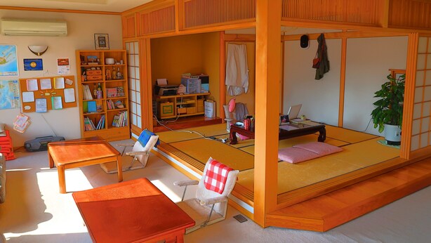 A traditional Japanese-style room with tatami flooring, a low wooden bed frame, a desk with a chair, a bookshelf, and a potted plant. - Otaru Ekimae Guest House Ito - Hostel (Otaru)