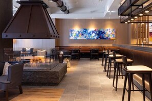 A modern restaurant with a stone fire feature, wooden seating, and a colorful abstract wall art.