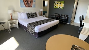 Una habitación de hotel con una cama grande, dos mesitas de noche, un escritorio con una silla, una mesa redonda y un cuadro en la pared.