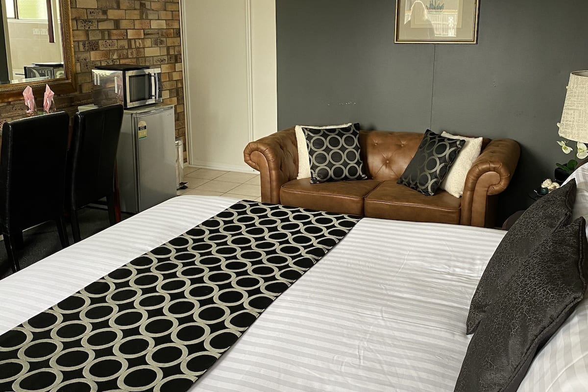 A hotel room with a large bed, a brown leather sofa, a microwave, and a refrigerator.