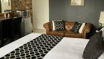 A hotel room with a large bed, a brown leather sofa, a microwave, and a refrigerator.