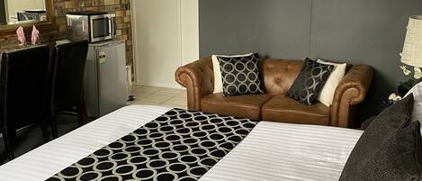 A hotel room with a large bed, a brown leather sofa, a microwave, and a refrigerator.