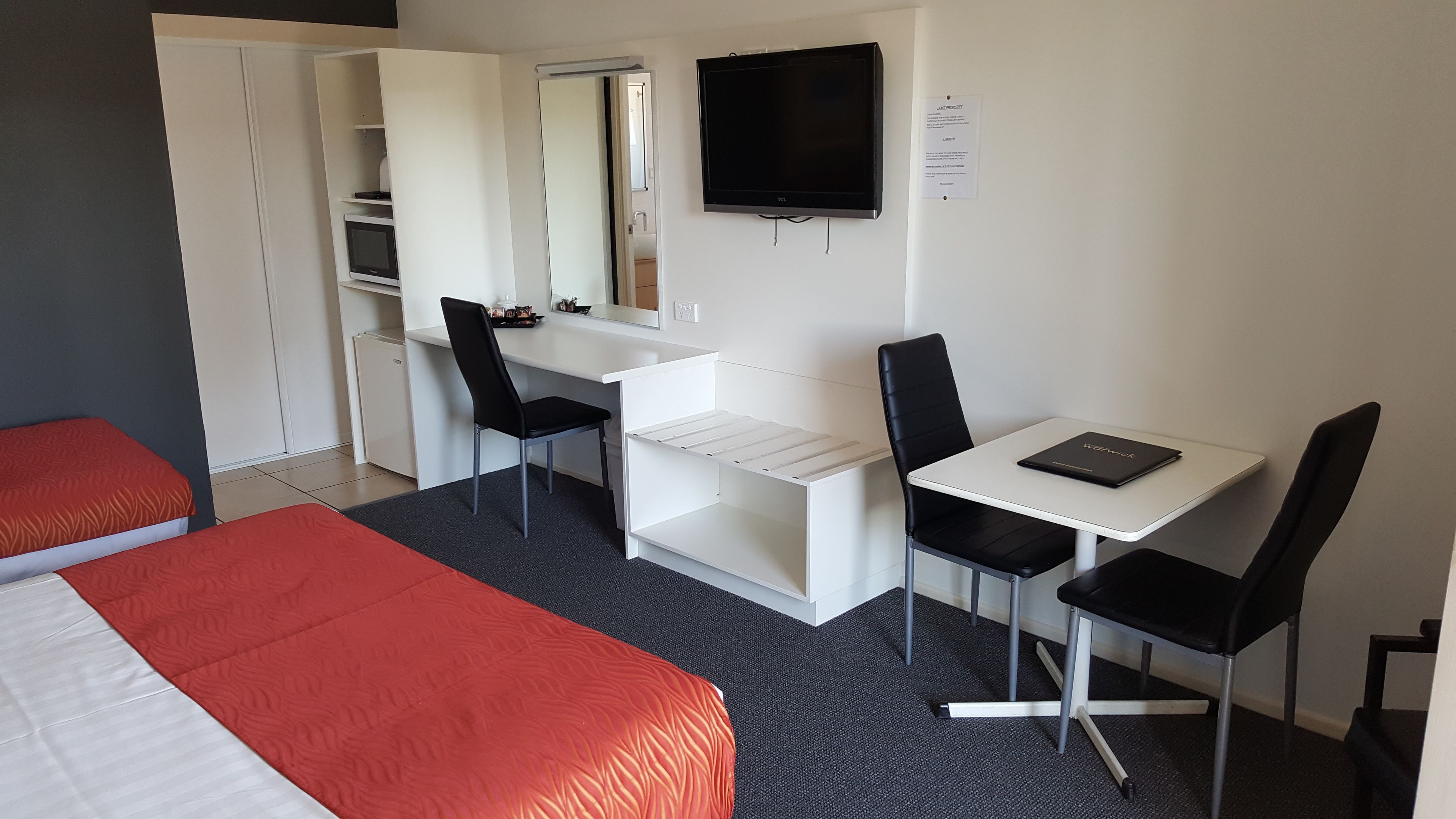 A hotel room with a bed, a desk with a chair, a TV, and a wardrobe.